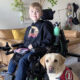 blond boy sitting in wheelchair with yellow Lab service dog sitting next to him
