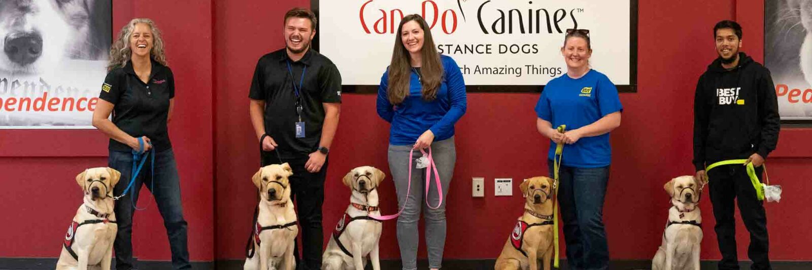 Group of six people all posing with dog in from of Can Do Canines logo.