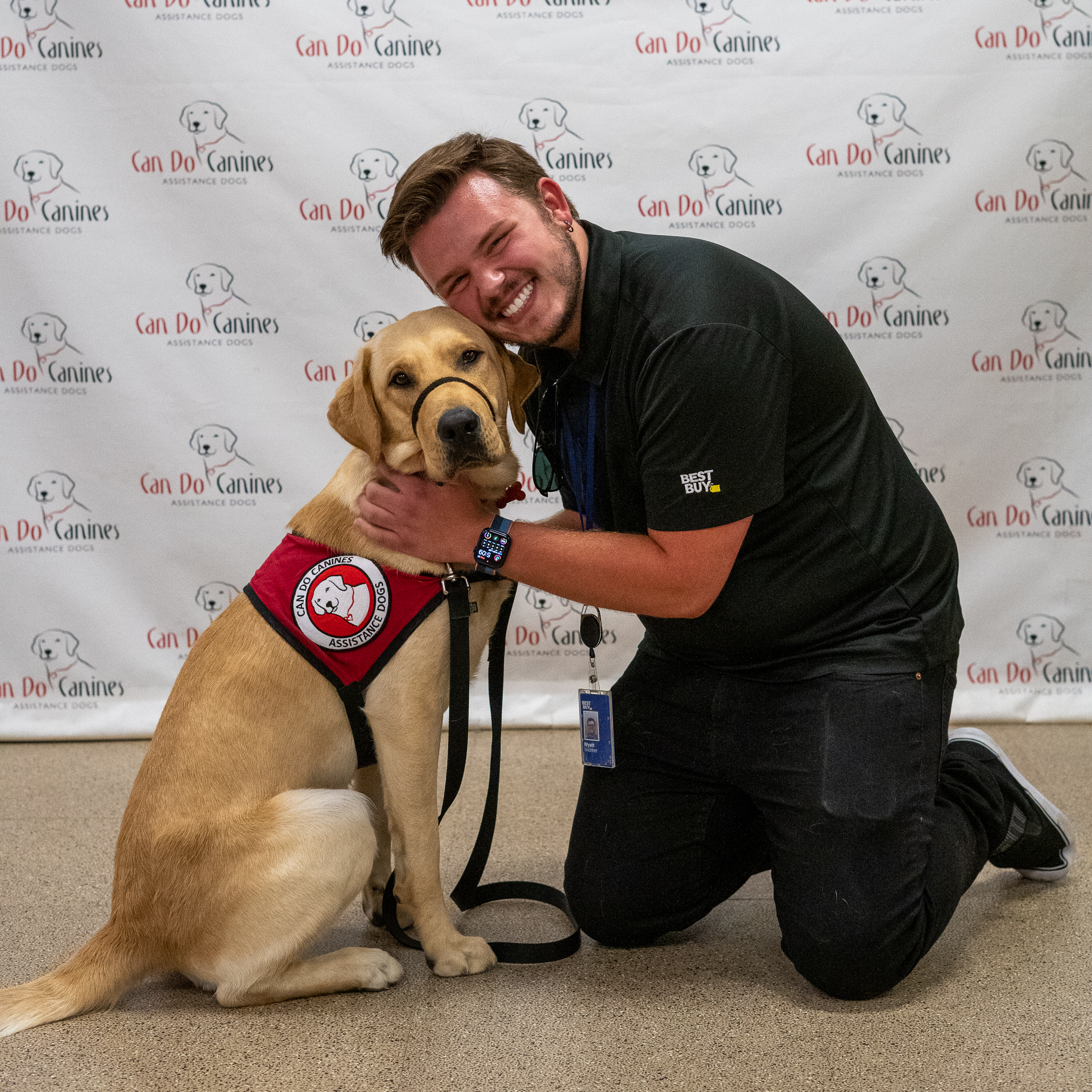 Man posing with a yellow Lab wearing a red Can Do Canines service dog vest