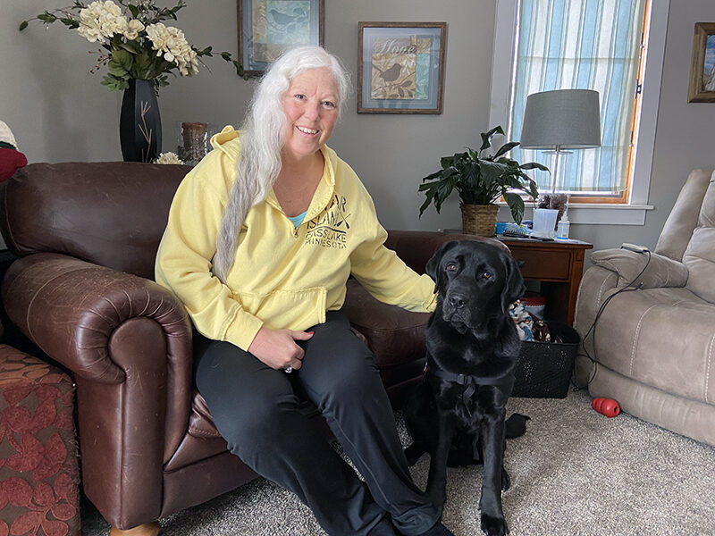 woman sitting in leather chair with black Lab sitting on floor in front of her