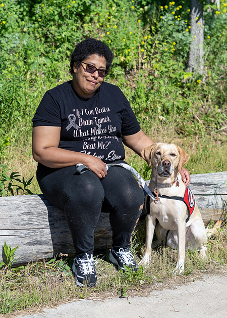 woman sitting on fallen log with yellow Lab service dog sitting next to her