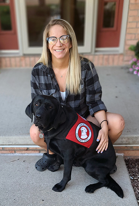 young woman with long blond hair sitting on front step with black Lab