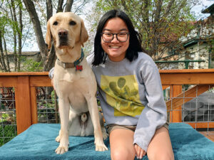 young woman sitting on outdoor bench with yellow Lab dog next to her