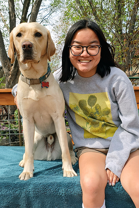 young woman sitting on outdoor bench with yellow Lab dog next to her