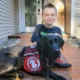 boy sitting on front sidewalk with black Lab dog wearing Can Do Canines assistance dog cape