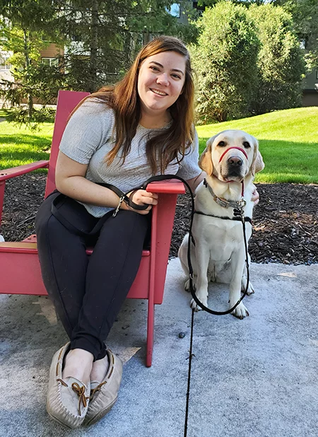 young woman sitting in wooden lawn chair with yellow Lab dog sitting on patio next to her