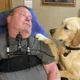 man sitting in wheelchair with yellow Lab dog sitting next to him and putting paw on his shoulder