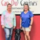 Two women and black Lab standing in front of Can Do Canines sign