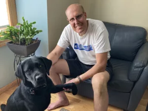 man sitting on leather sofa with black Lab sitting on front in front of him