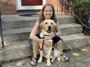 young woman sitting on front steps and hugging yellow Lab dog from behind
