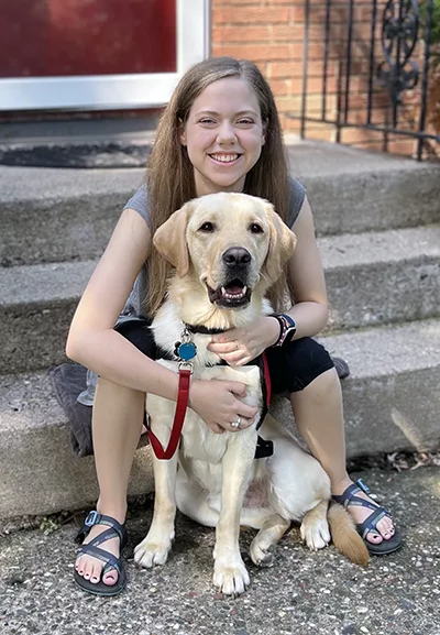 young woman sitting on front steps and hugging yellow Lab dog from behind