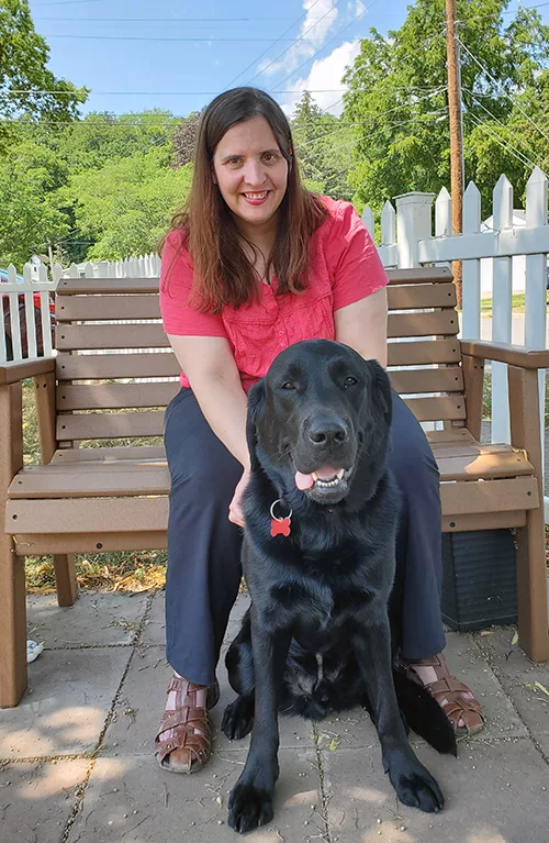 woman sitting on outside porch swing with black Lab dog sitting in front of her
