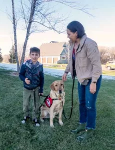 young boy with his yellow Lab and mom in a grassy area