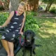 Woman sitting in powerchair, with black Lab sitting on lawn beside her