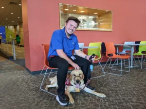 Man sitting in a chair with a yellow Lab laying down under it.