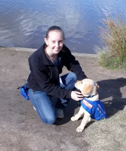 Young woman posting with a yellow lab puppy wearing a blue cape. 