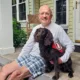man sitting on front step with arm around Spaniel dog wearing Can Do Canines service cape