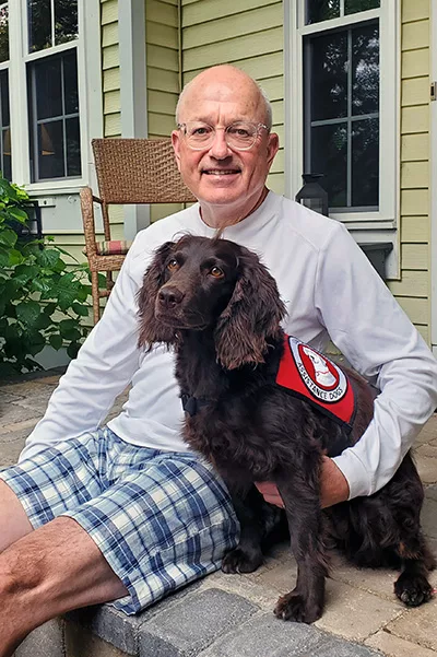 man sitting on front step with arm around Spaniel dog wearing Can Do Canines service cape