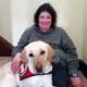 woman sitting on carpeted stairs with yellow Lab service dog lying with her