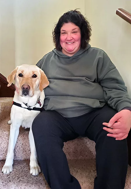 woman sitting on carpeted stairs with yellow Lab service dog lying with her