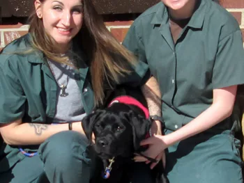 Women inmates posing with a black Lab puppy