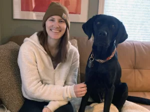 woman and black Lab dog sitting side by side on sofa