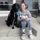 young woman sitting on front steps with black Lab dog wearing service cape sitting next to her