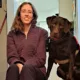 woman and chocolate Lab dog sit together at top of inside stairs smiling at camera