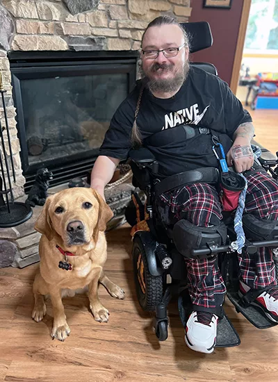 man sitting in wheelchair next to yellow Lab dog and both are looking at the camera