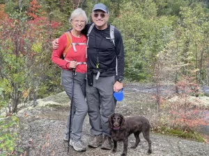 couple with small dog all standing on hiking trail smiling at camera