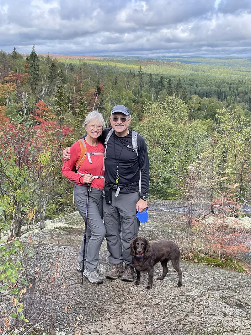 couple with small dog all standing on hiking trail smiling at camera