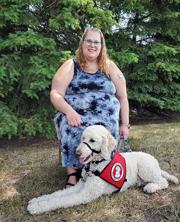 woman sitting outside with white Standard Poodle service dog lying in front of her