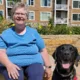 woman sitting on chair outside apartment building with black Lab dog sitting next to her
