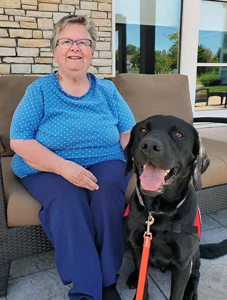 woman sitting on bench outside with black Lab dog sitting next to her