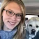young woman with blond hair and glasses smiling for selfie with yellow Lab in back seat of car behind her