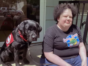woman and black Lab service dog sitting on front steps of home