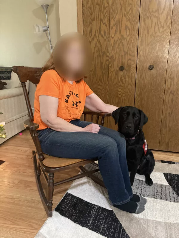 person sitting next to black Lab service dog