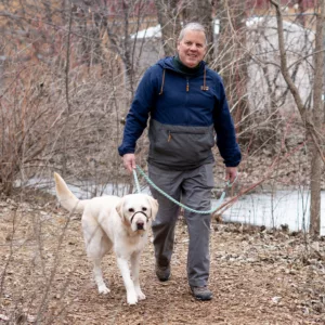 Man walking with a yellow Labrador in a wooded area.