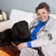 Smiling woman sitting on sofa with arms around black Lab lying on her lap