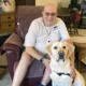 man sitting on recliner with hands on yellow Lab service dog sitting in front of him