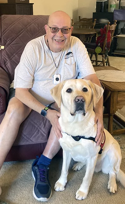 man sitting on recliner with hands on yellow Lab service dog sitting in front of him