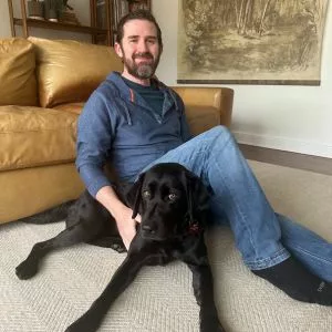 man sitting on a living floor with a black Lab