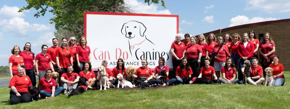 Can Do Canines staff posing in front of the Facility sign outside.