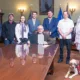 group of adults standing in formal room behind large table with one man sitting at table holding up document and with yellow Lab service dog lying on ground near table