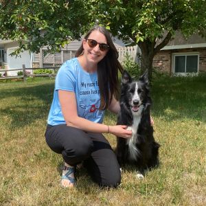 Woman wearing a blue race team shirt kneeling next to a black and white border collie