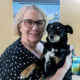 woman holding small black, white, and tan dog in living room; both are smiling at camera