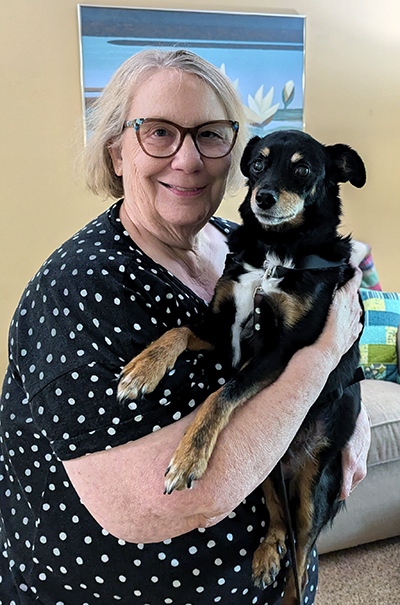 woman holding small black, white, and tan dog in living room; both are smiling at camera