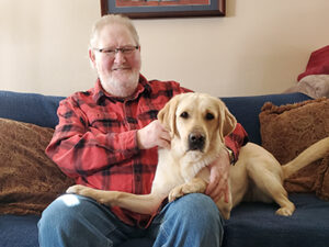 man sitting on sofa with arms around yellow Lab dog sitting across his lap