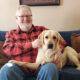 man sitting on sofa with arms around yellow Lab dog sitting across his lap