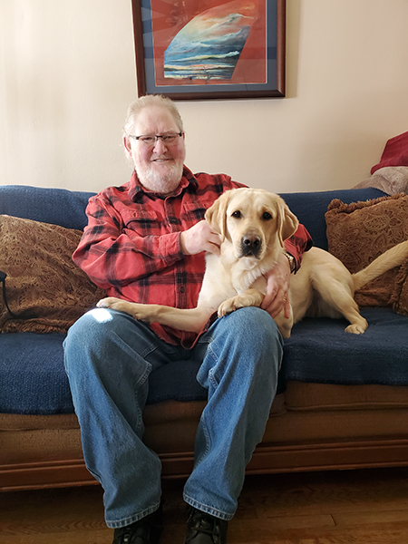 man sitting on sofa with arms around yellow Lab dog sitting across his lap